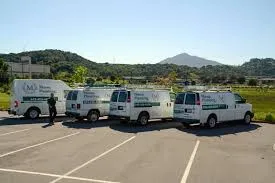 A row of Mason Plumbing, Inc. service vans parked in a lot in San Anselmo, with a scenic backdrop of hills and a mountain.
